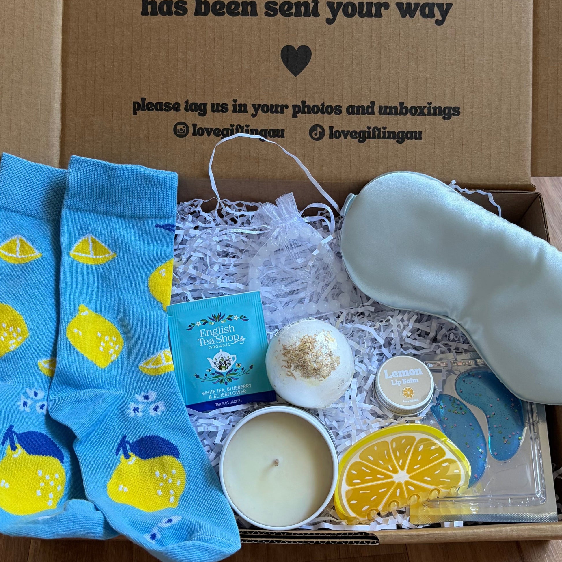 Gift box with blue lemon-sleeve socks, candles, and other items on a wooden floor.
