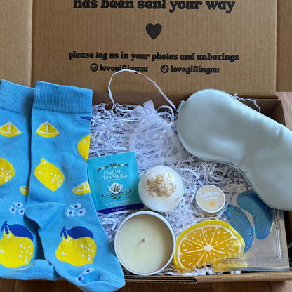 Gift box with blue lemon-sleeve socks, candles, and other items on a wooden floor.