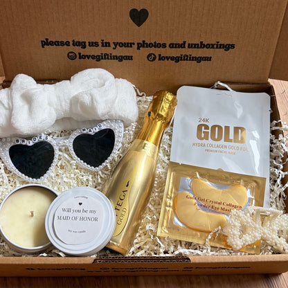 Gift box with a bottle of champagne, candle, and other items on a wooden surface.
