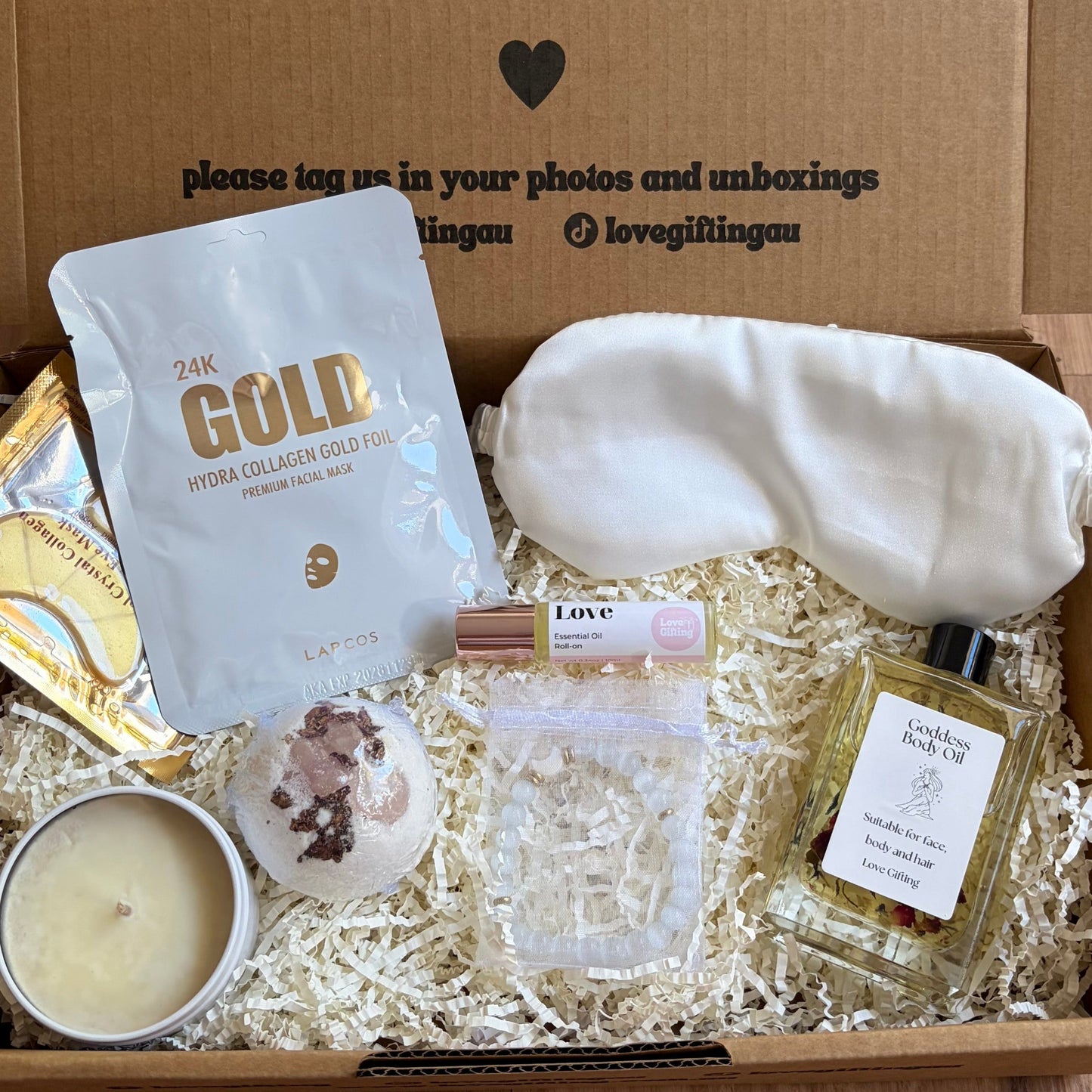 Gift box with various items including a candle, soap, and a bag labeled 'The Gold' on a wooden surface.