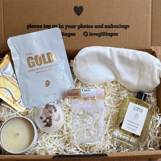 Gift box with various items including a candle, soap, and a bag labeled 'The Gold' on a wooden surface.
