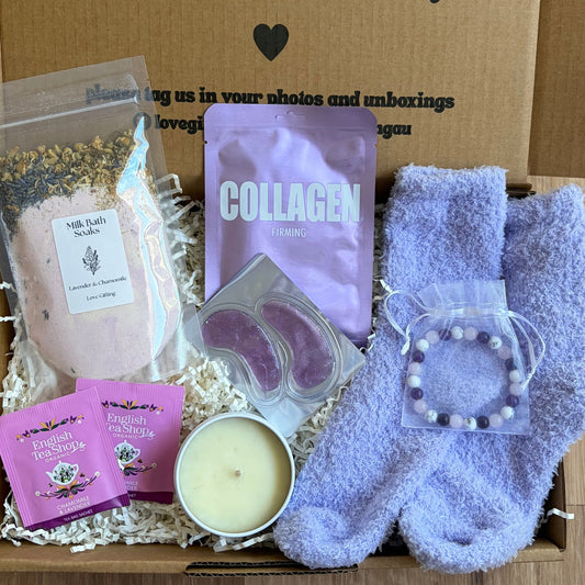 Box of self-care items including socks, a candle, and packets with text on a wooden surface.