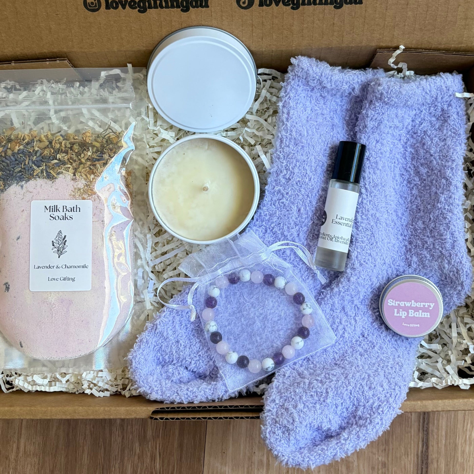 Box of sleep self-care items including a candle, soap, and bathrobe on a wooden surface.