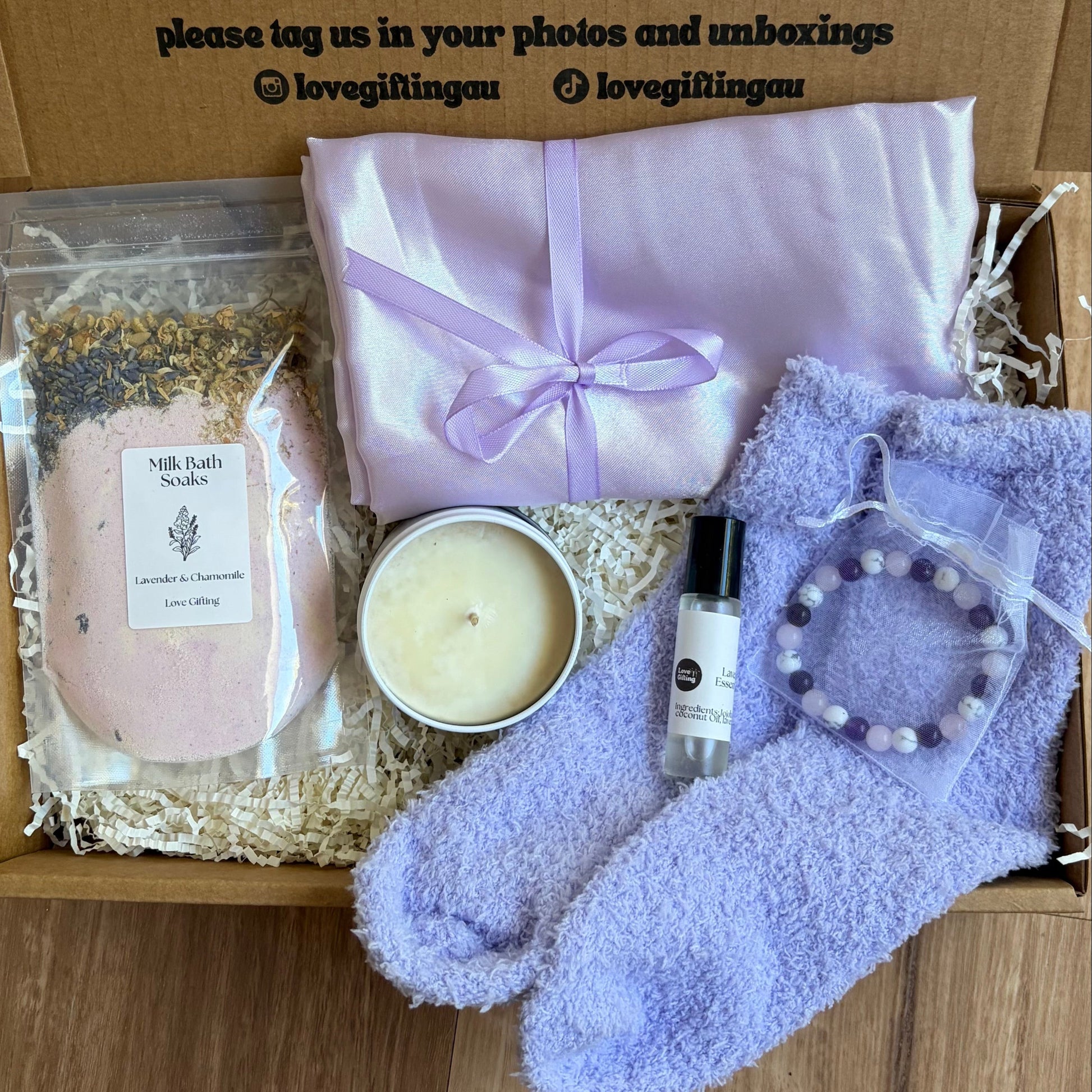 Gifting box with lavender-themed items including a candle, soap, and socks on a wooden surface.
