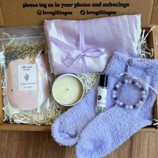 Gifting box with lavender-themed items including a candle, soap, and socks on a wooden surface.