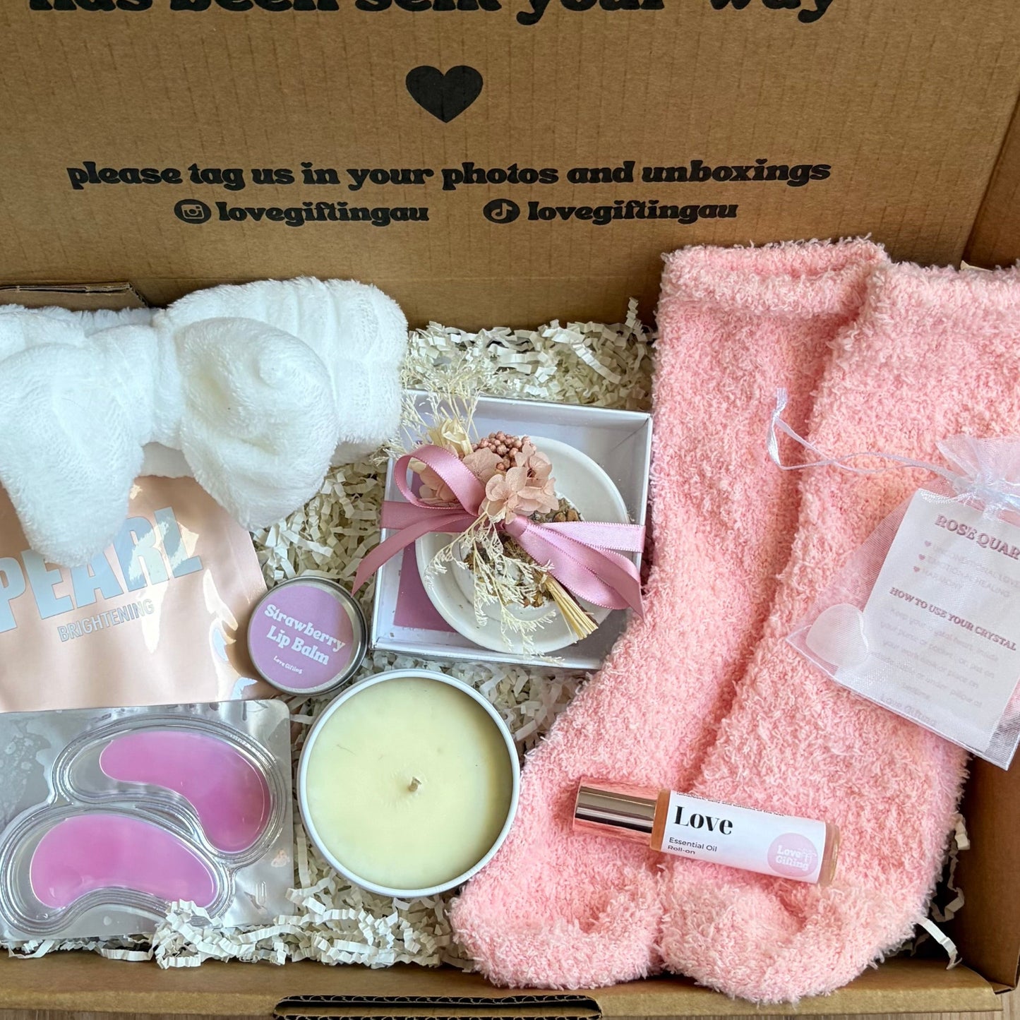 Gift box with pink towel, candle, and other items on a wooden surface