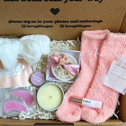 Gift box with pink towel, candle, and other items on a wooden surface