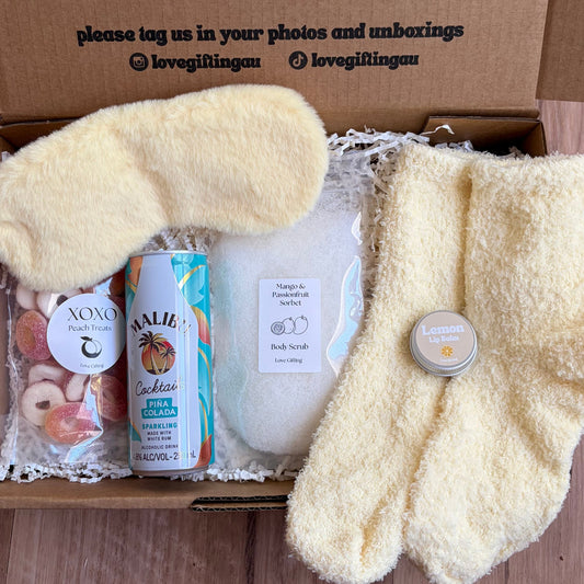 Gift box with plush socks, bath bombs, and a candle on a wooden surface.