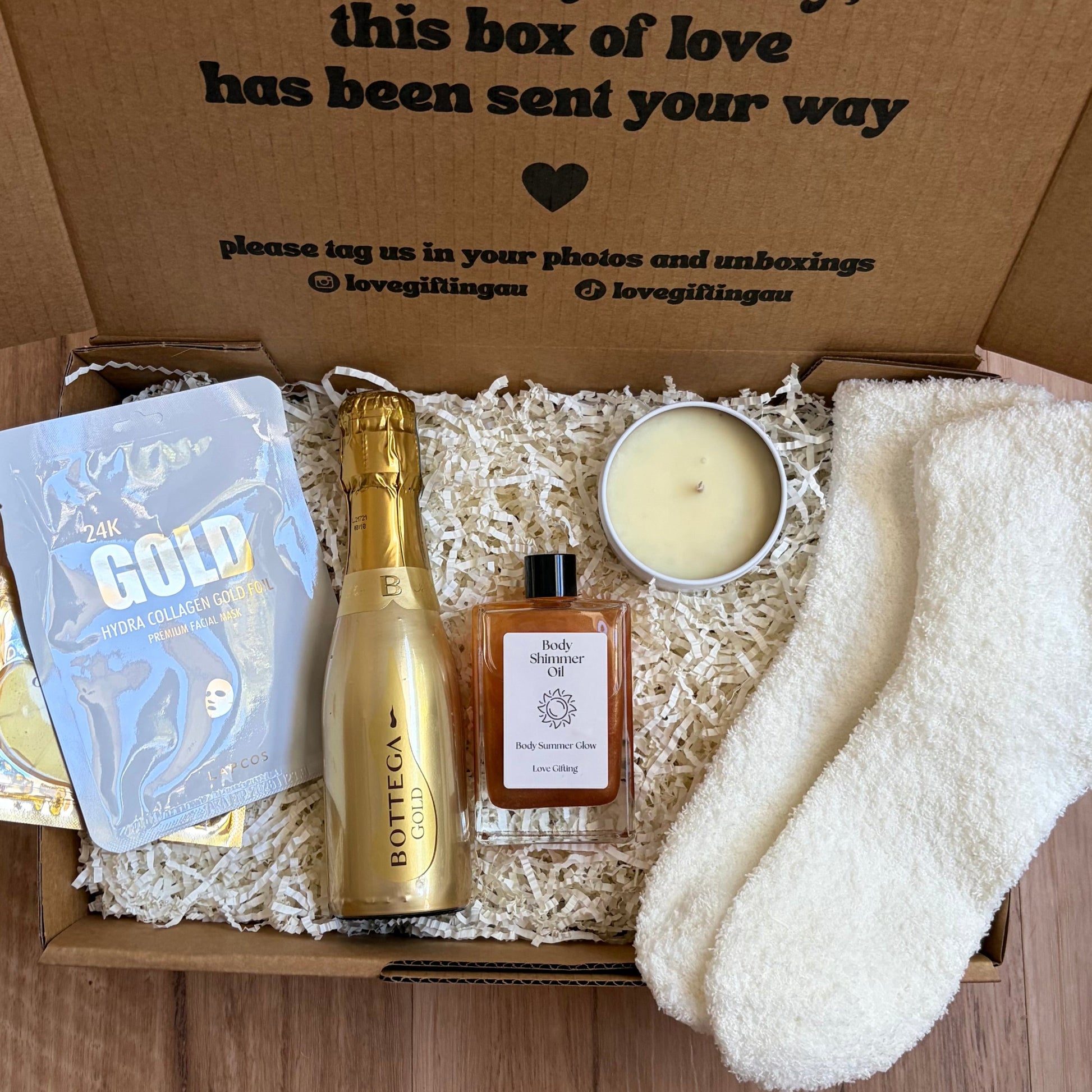 Gift box with a bottle of champagne, candle, and other items on a wooden surface.