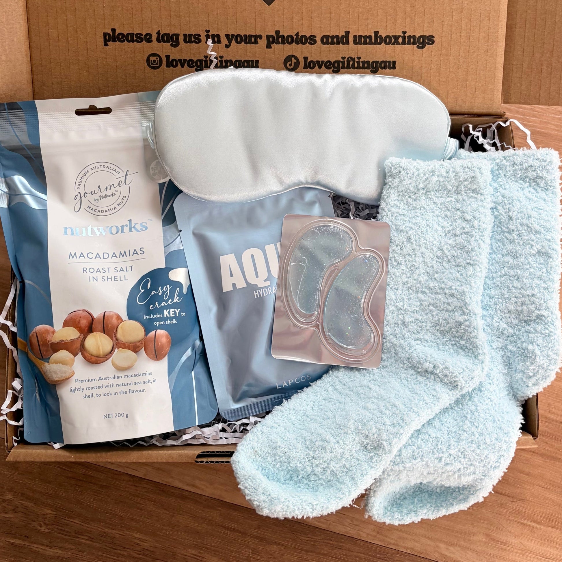 Box of assorted items including socks, macadamia nuts, and a face mask on a wooden surface.