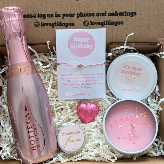 Gift box with pink bottle, card, and candles on a wooden surface