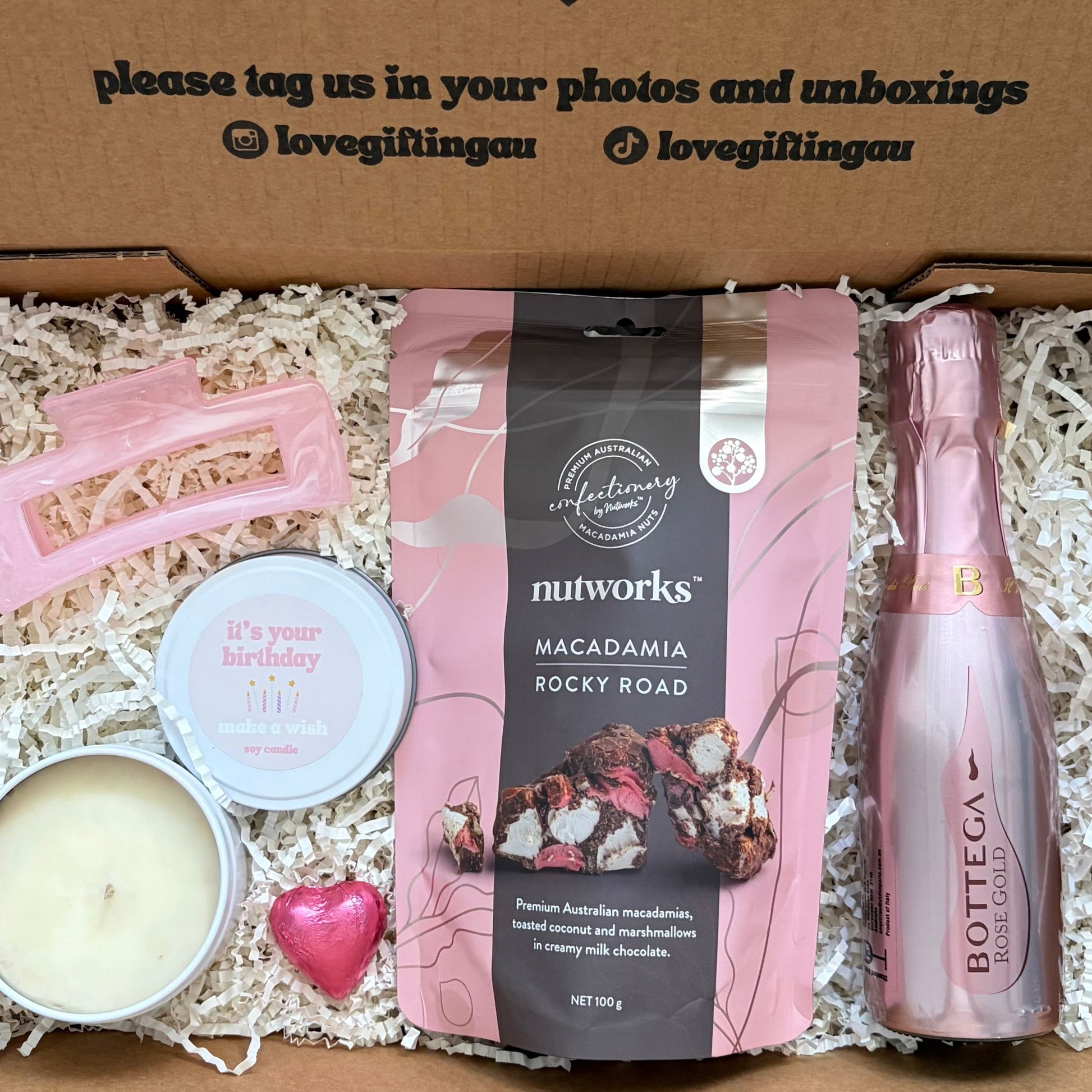 Gift box with a bottle of Prosecco, macadamia rocky road, and a candle, with a message on the lid.
