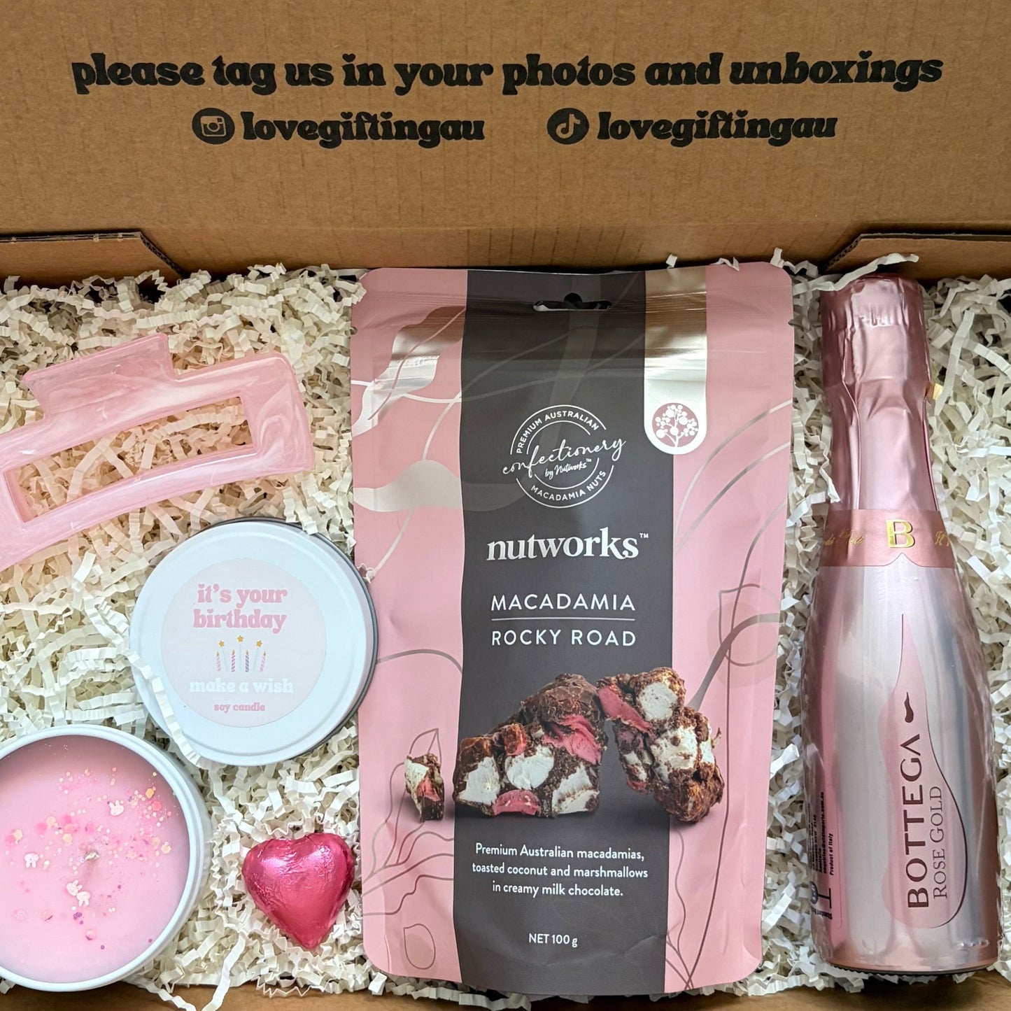 Gift box with pink bottle, macadamia nuts, and other items with a message on the lid.