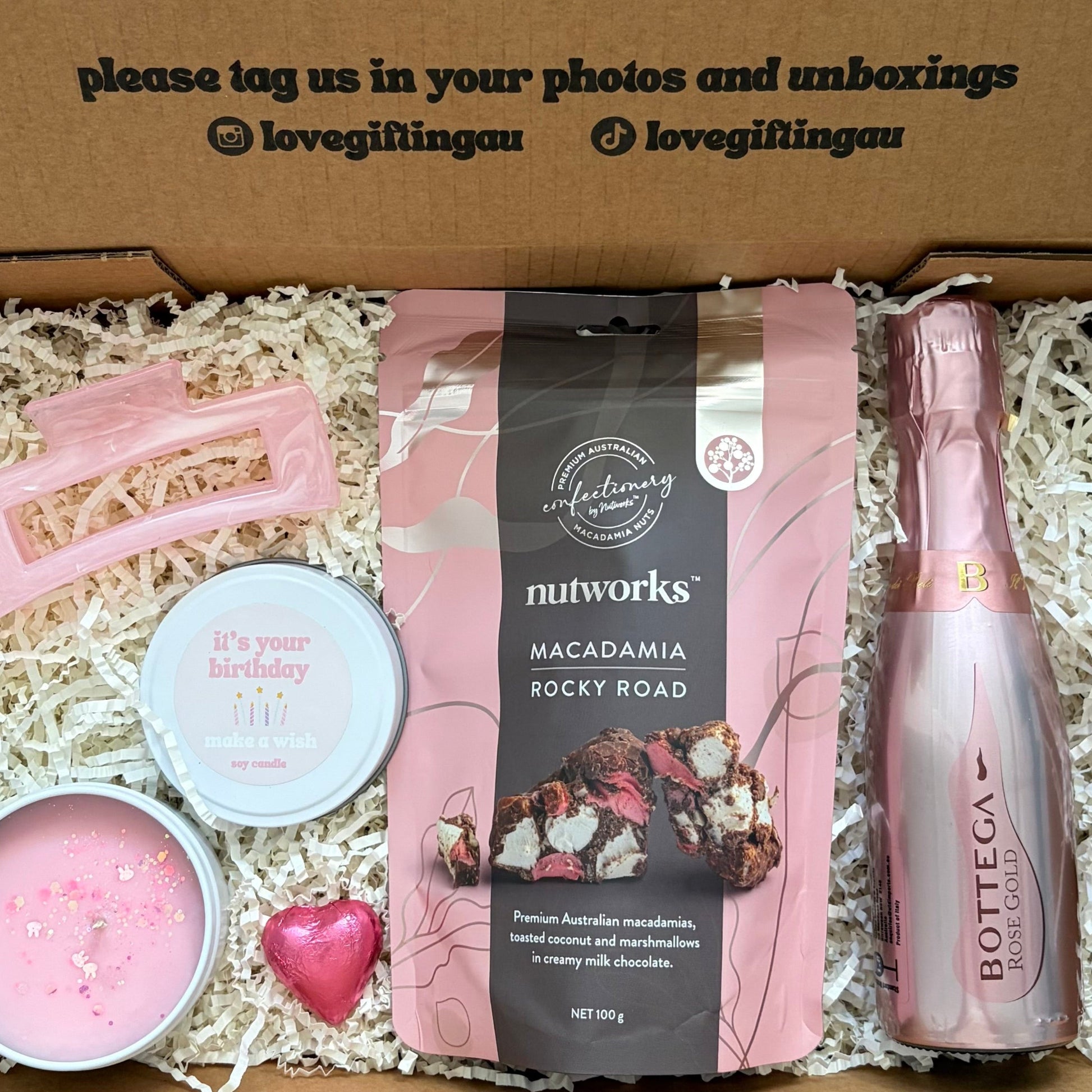 Gift box with pink bottle, macadamia nuts, and other items with a message on the lid.