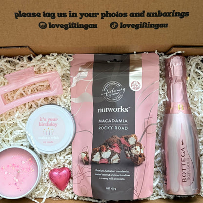 Gift box with pink bottle, macadamia nuts, and other items with a message on the lid.