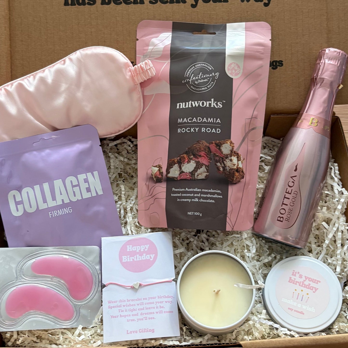 Gift box with various items including a bottle, candle, and packets on a wooden surface.