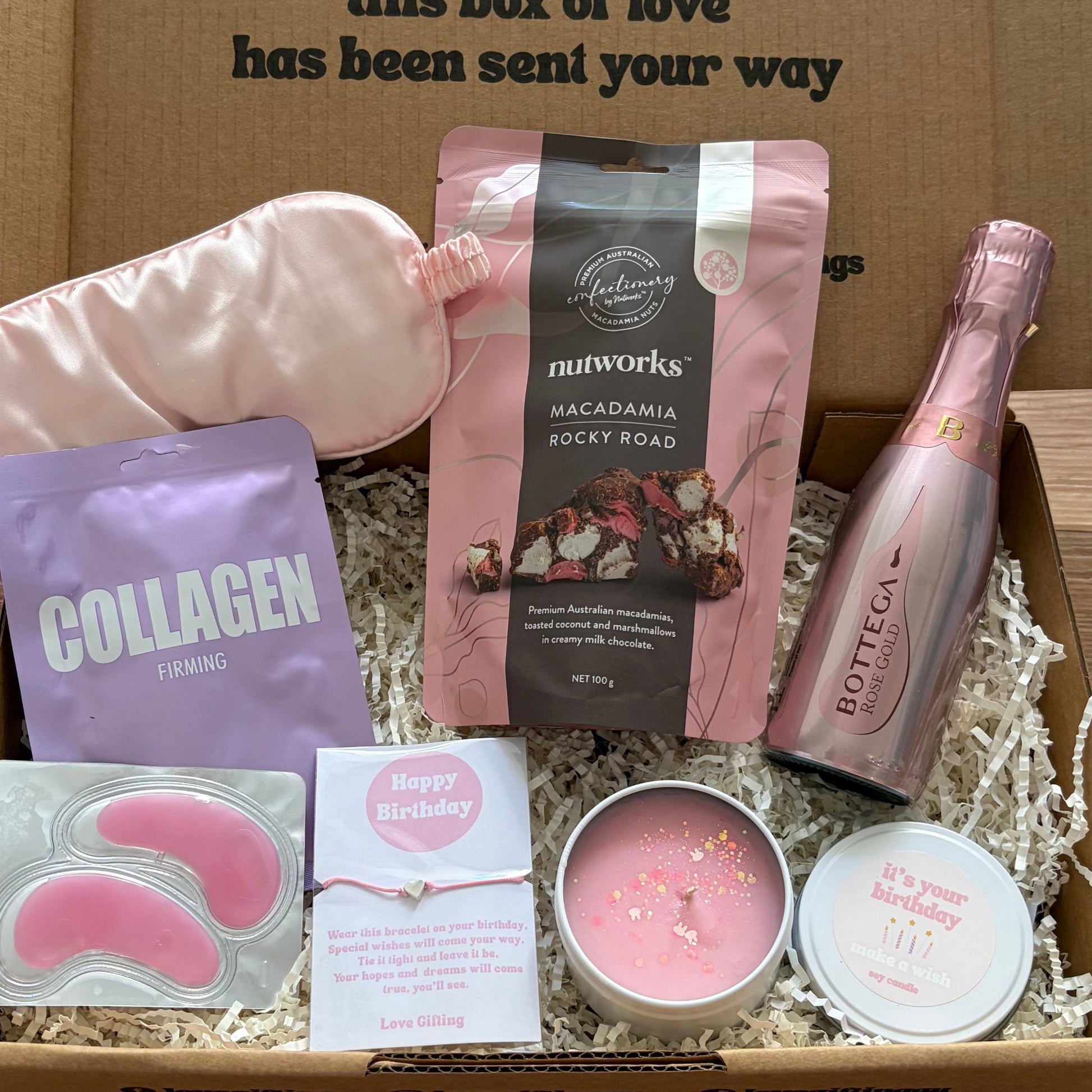 Gift box with self-care items including a bottle, skincare products, and a candle on a wooden surface.