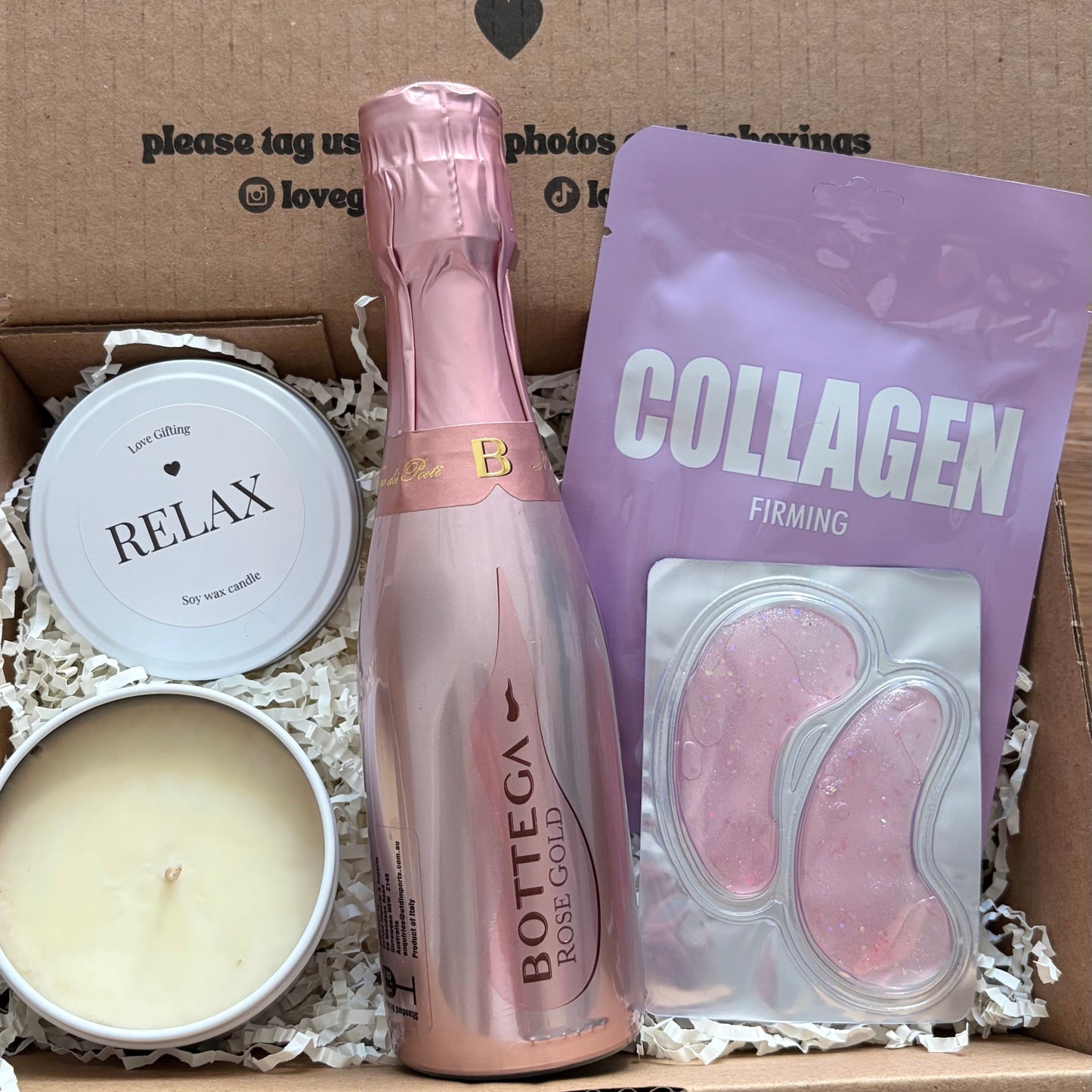 Gift box with Bottega Rose bottle, candle, and collagen packaging on a wooden surface.