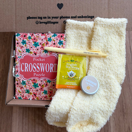Box of love with a crossword puzzle, tea, and socks on a wooden surface
