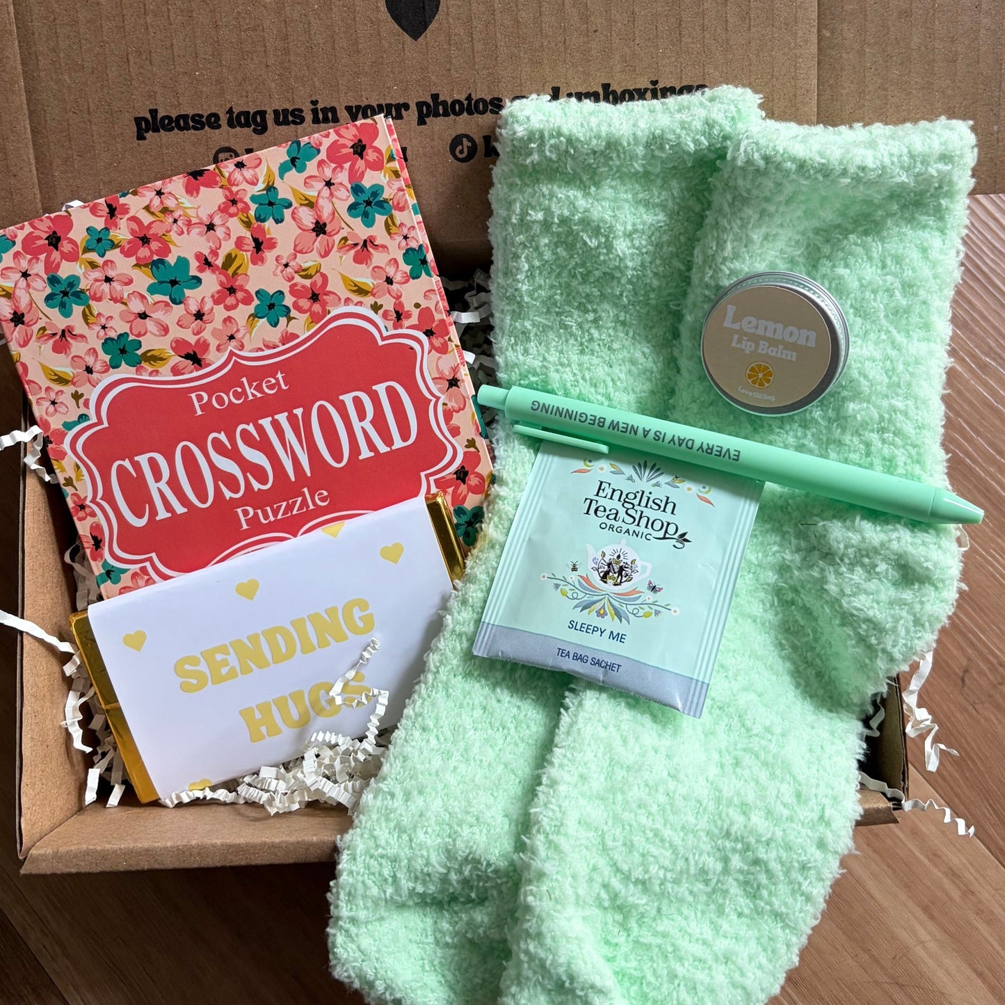 Box of care with light green socks, crossword puzzle, and other items on a wooden surface.