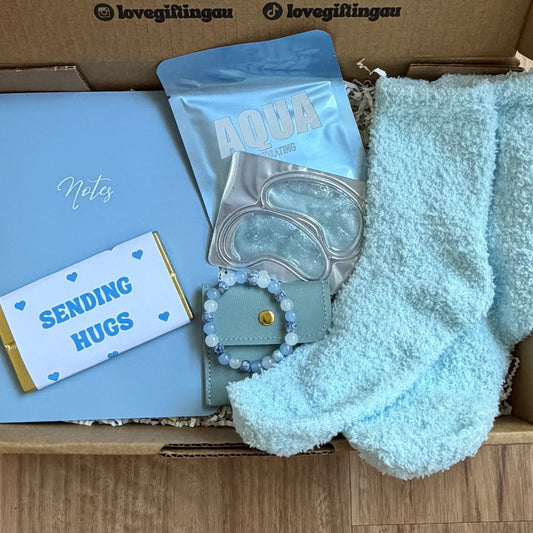 Box of care package with a card, socks, and other items on a wooden surface.