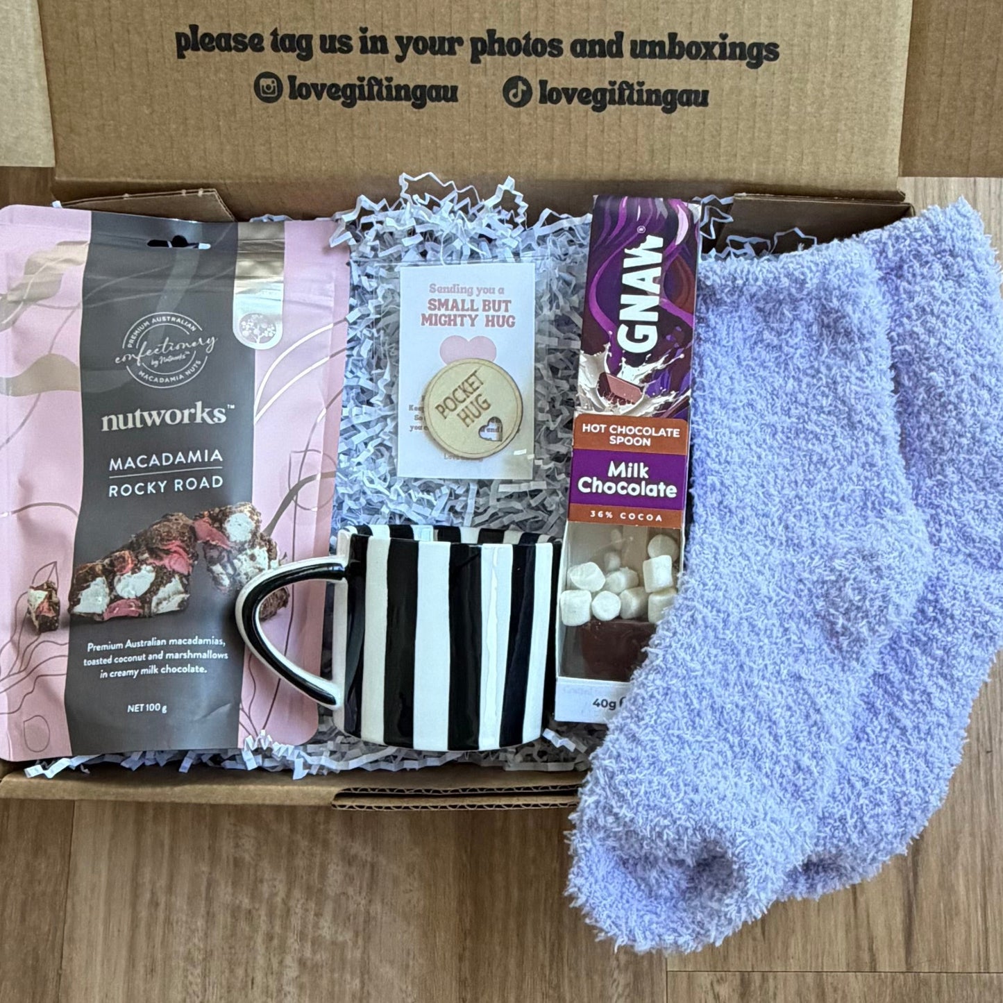 Gift box with socks, mug, and other items on a wooden surface