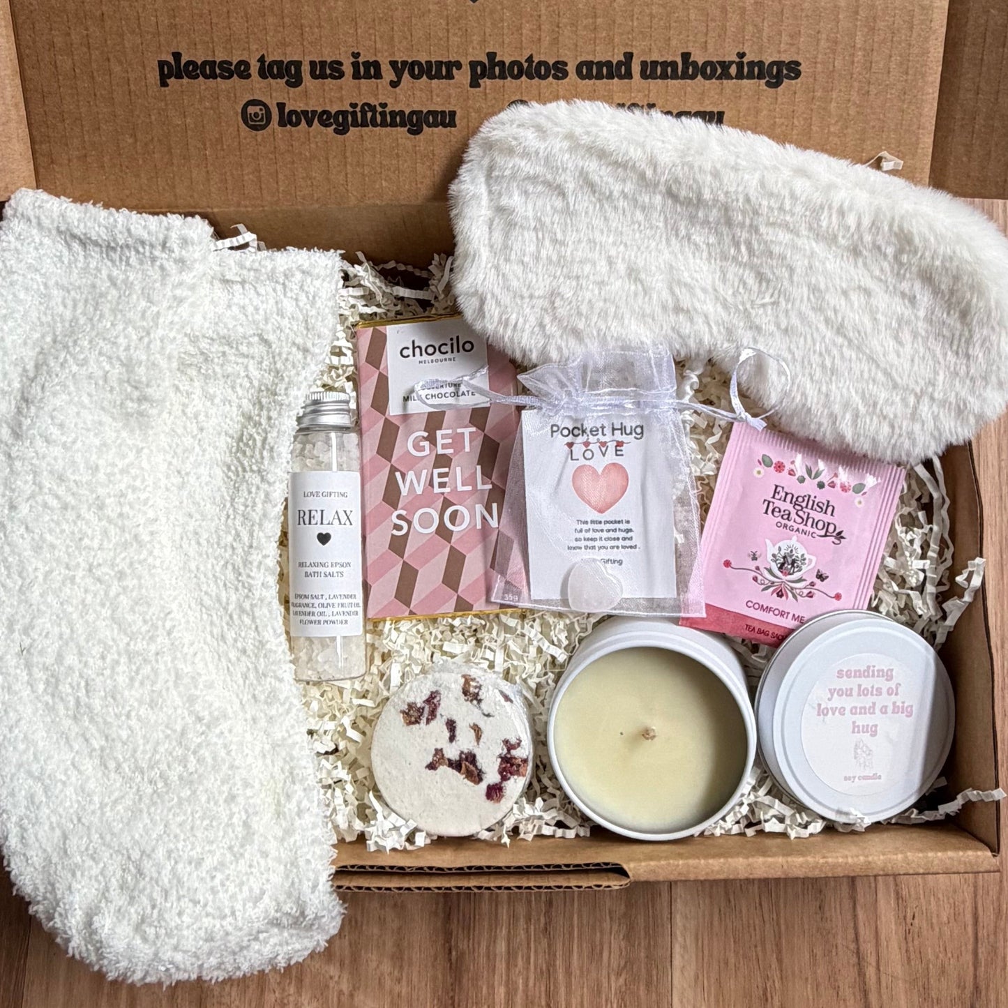 Gift box with products and a blanket on a wooden surface, featuring a personalized message.