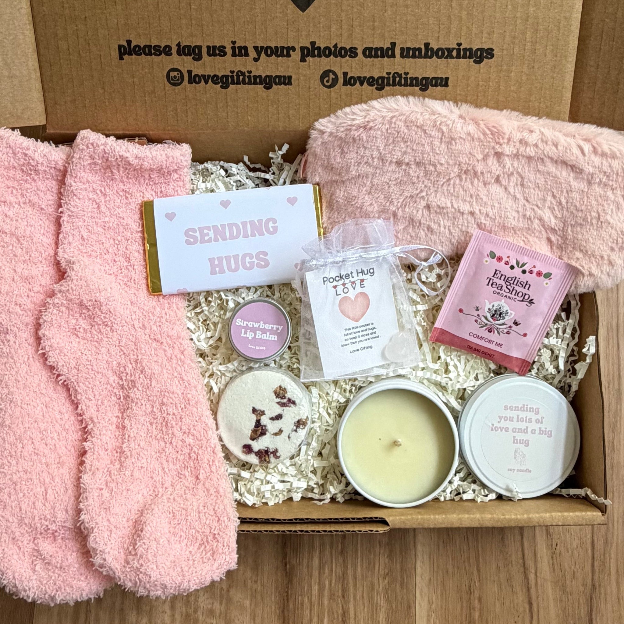 Gift box with pink socks, candles, and cards on a wooden surface