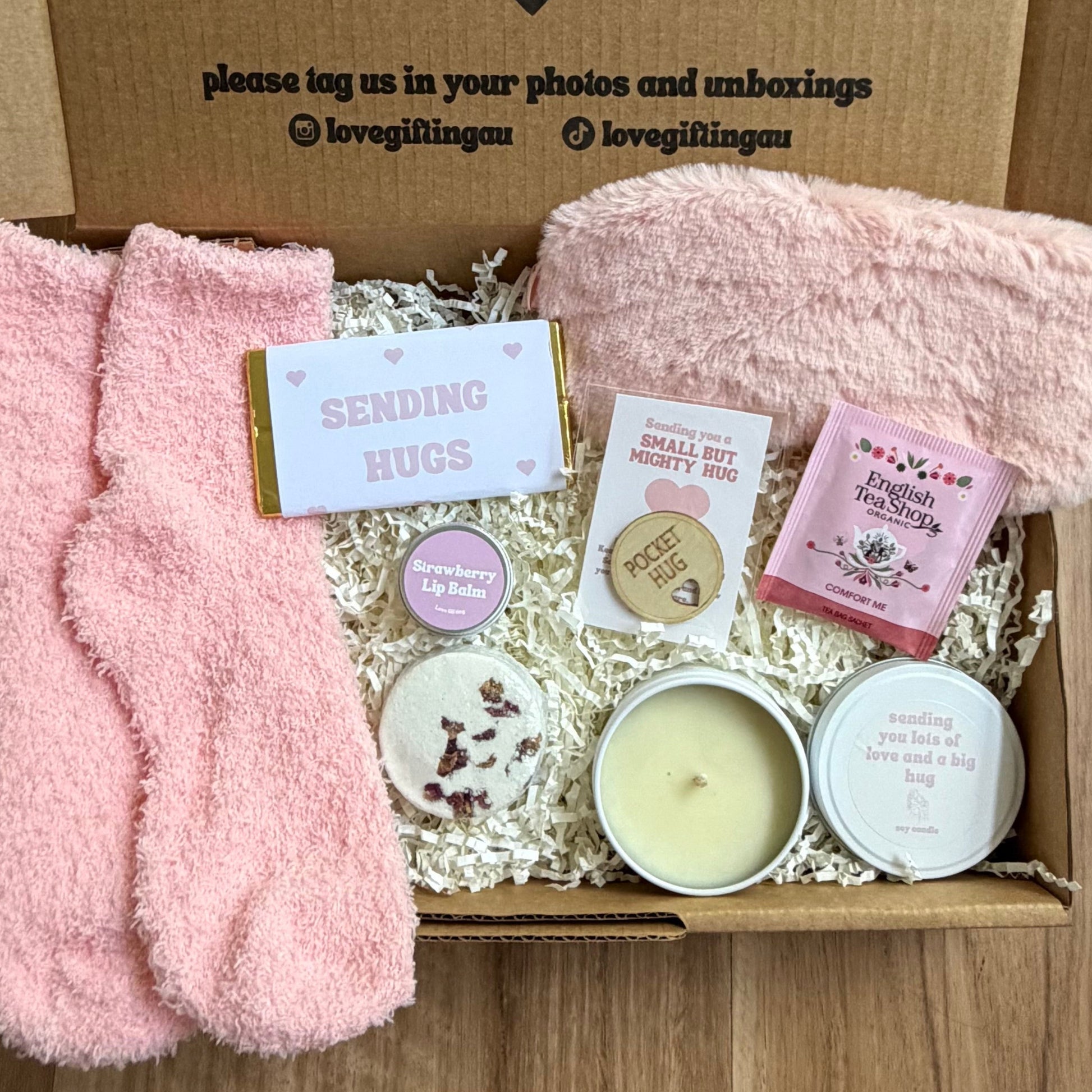 Gift box with pink socks, candles, and other items on a wooden surface