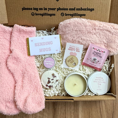 Gift box with pink socks, candles, and other items on a wooden surface