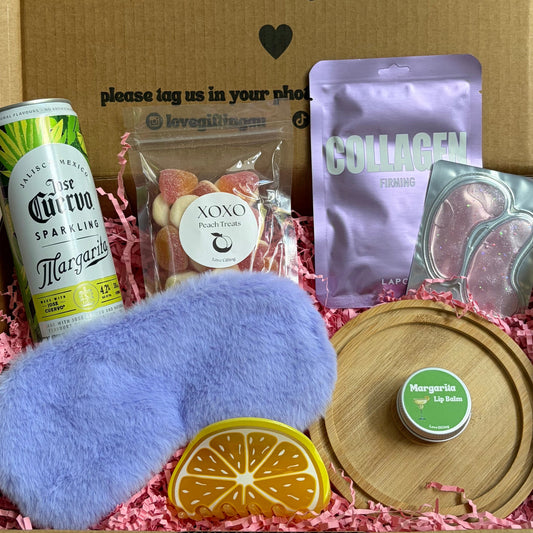 Gift box with various items including a can of beer, a plush toy, and a bottle cap on a wooden surface.