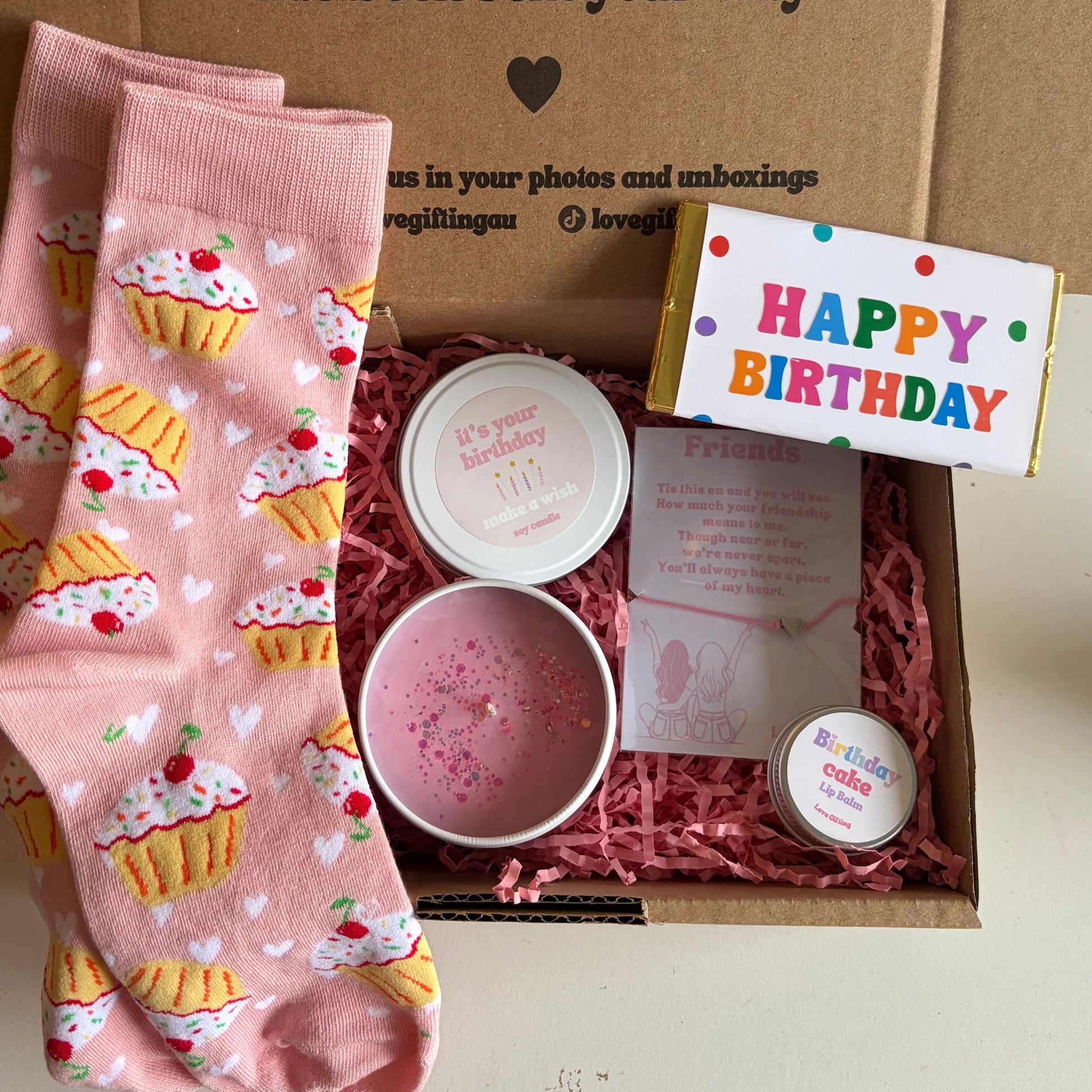 Birthday gift set with pink cupcake-patterned socks, a small bowl, and a 'Happy Birthday' card in a box.