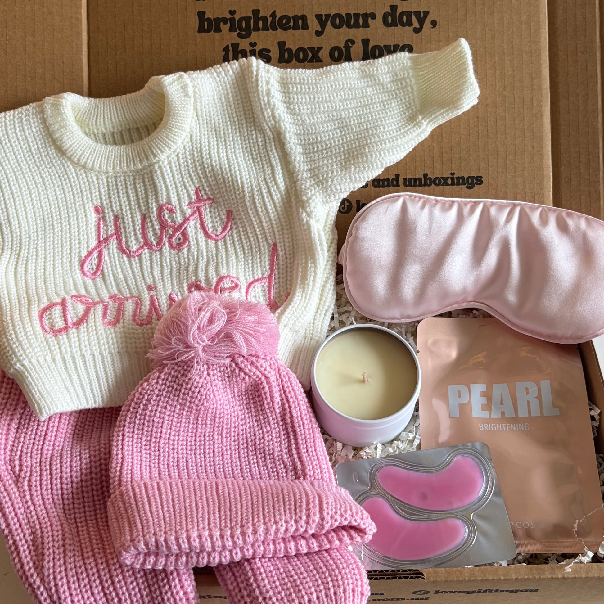 Gift box with a sweater, hat, leggings, candle, and eye mask on a white surface.