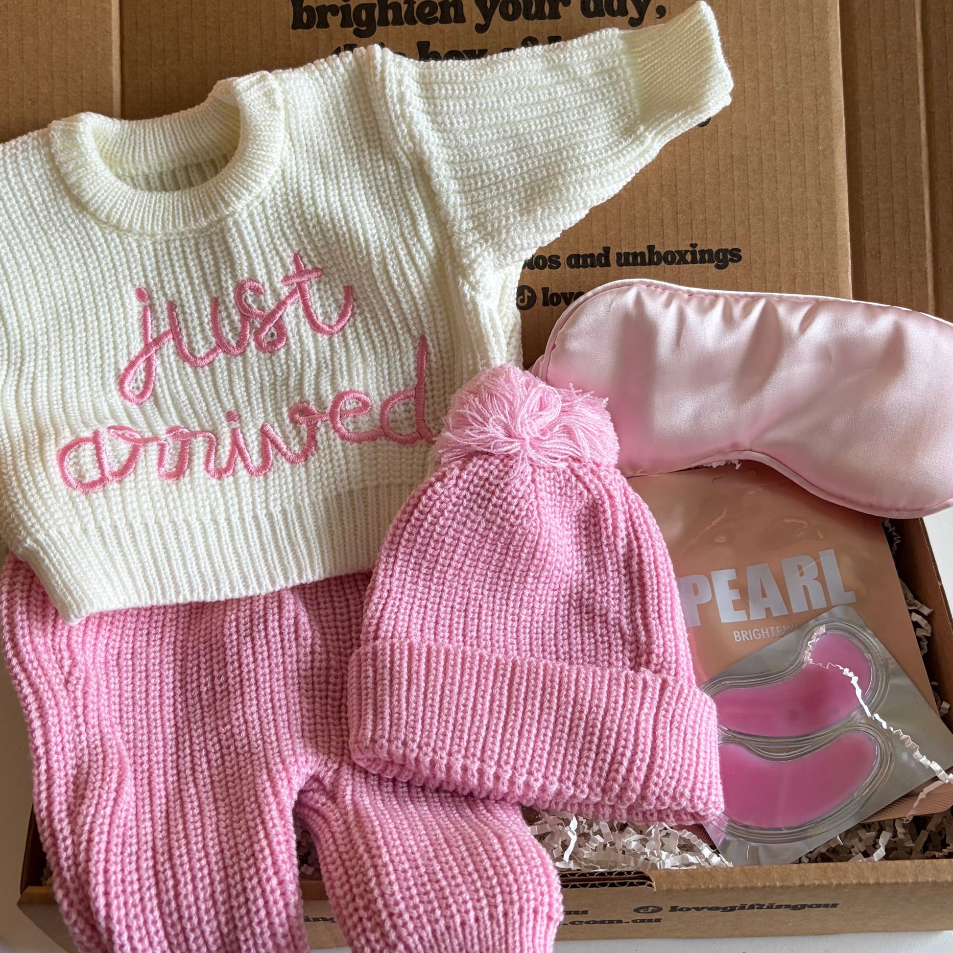 Baby outfit with 'just arrived' sweater, pink hat, and pants on a box.