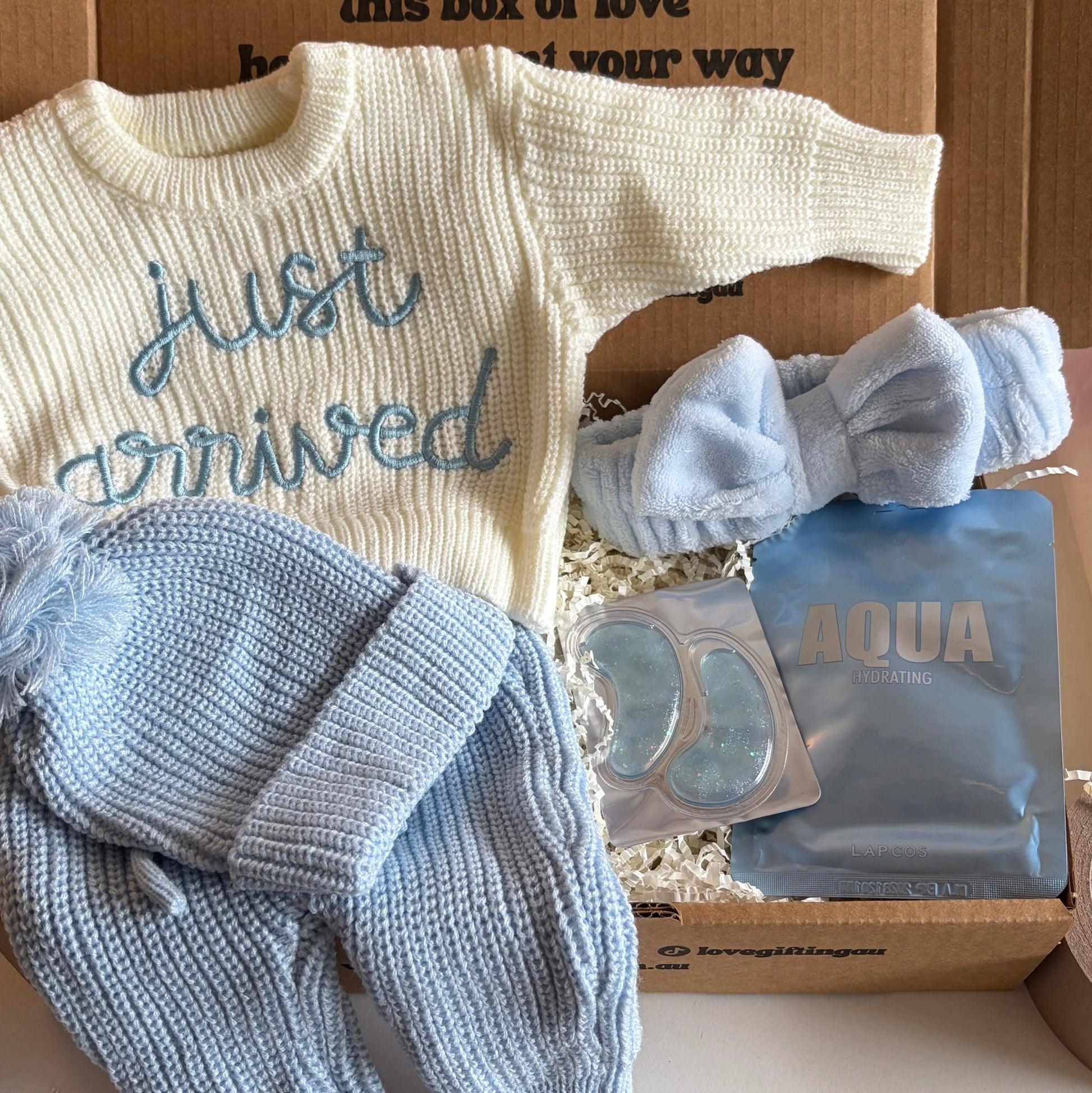 Baby outfit with 'just arrived' sweater, pants, and hat in a box with text.