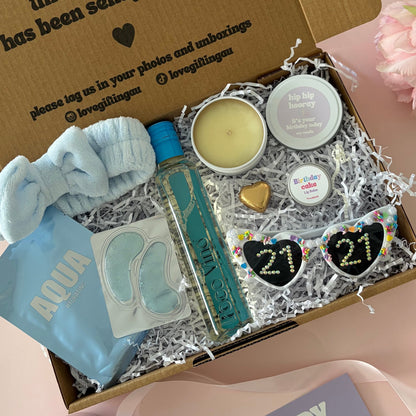A curated 30th birthday gift box . The box contains a light blue baby headband a mini  bottle of sav blanc, a small candle, lapcos face mask , under eye mask ,lipbalm and age '30'  sunglasses 