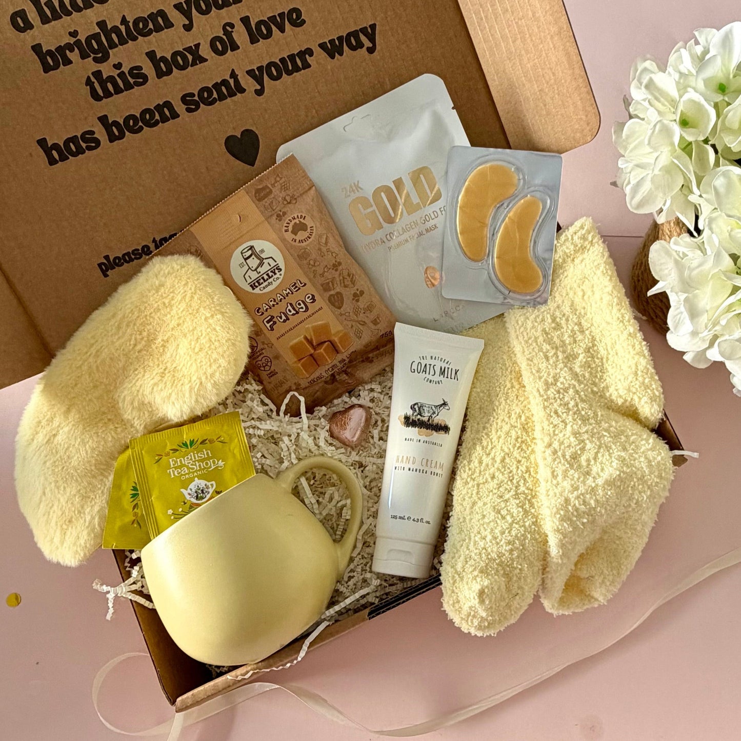 A curated comfort winter gift box featuring a yellow mug, lemongrass teabags, Kellys Candy Co Fudge, warm fluffy yellow socks, mini chocolate heart, yellow fluffy sleep mask and a tube of hand cream.  Lapcos Gold Facemask sheet and under eye gold masks.