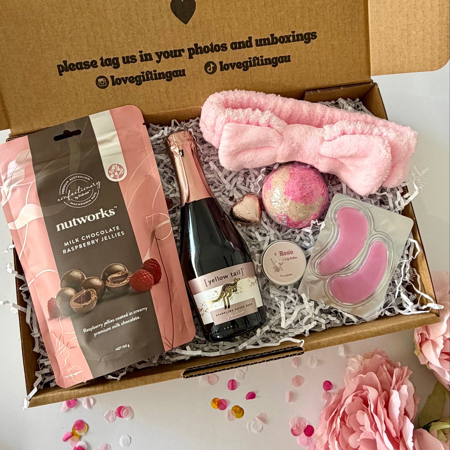A curated self care birthday or pamper gift box  includes nutworks chocolate-covered raspberry jellies, a pink towelling headband a strawberry bath bomb, Rosé prosecco, Rosé lipbalm and pink under eye masks.