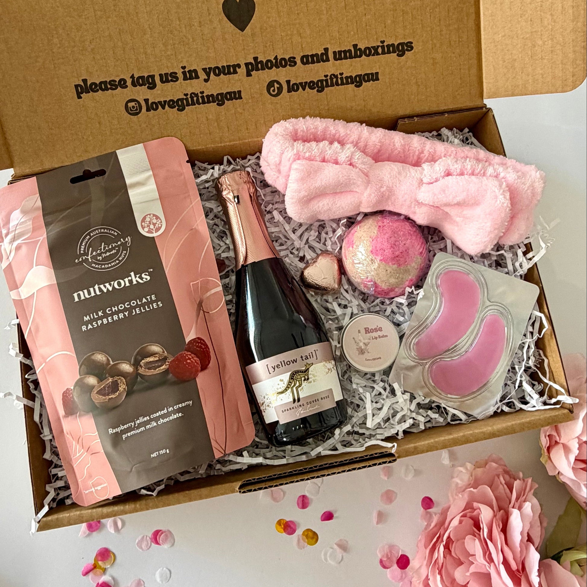 A curated self care birthday or pamper gift box  includes nutworks chocolate-covered raspberry jellies, a pink towelling headband a strawberry bath bomb, Rosé prosecco, Rosé lipbalm and pink under eye masks.