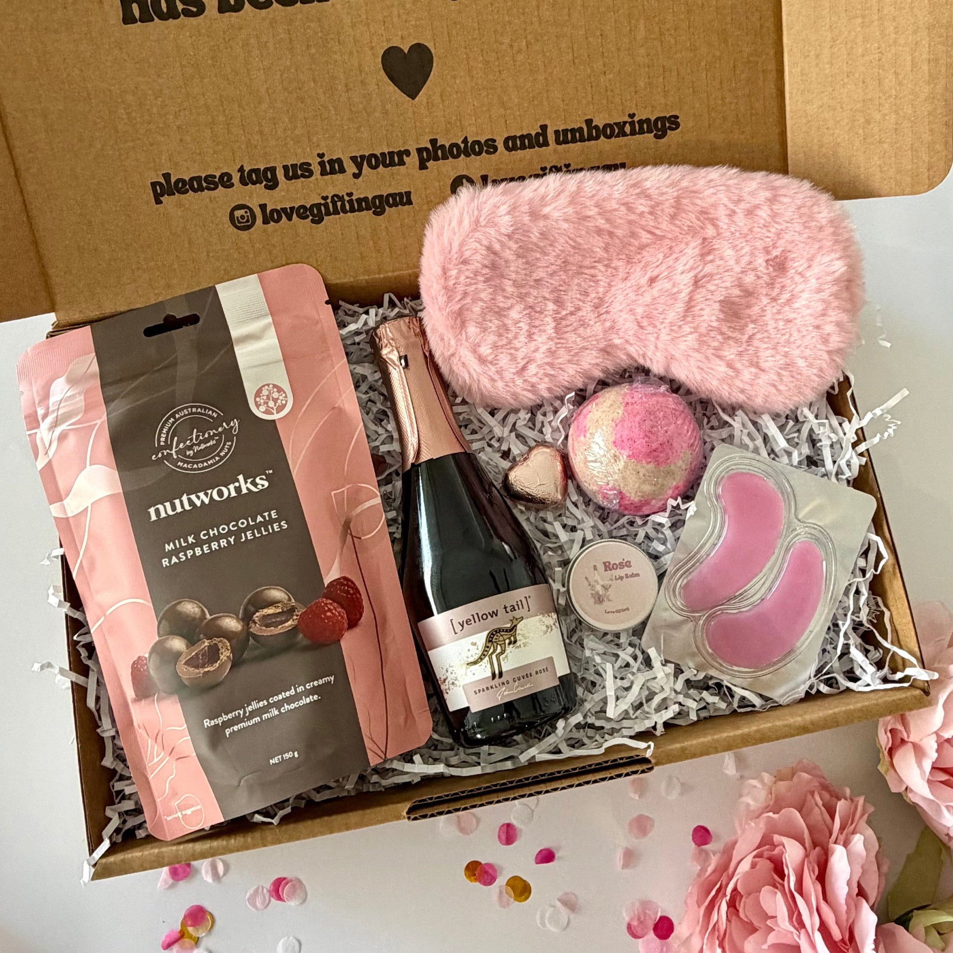 A curated self care birthday or pamper gift box  includes nutworks chocolate-covered raspberry jellies, a pink plush eye mask, a strawberry bath bomb, Rosé prosecco, Rosé lipbalm and pink under eye masks.