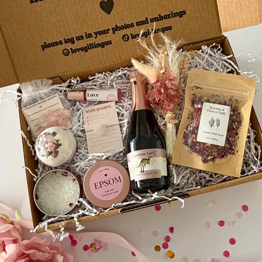 A curated  pamper self-care gift box set includes  a mini bottle of Rosé Prosecco , a rose quartz bath bomb, a tin of Epsom salts, a pouch of dried flowers, rose quartz hug, rose quartx bracelet and Love essential oil roller