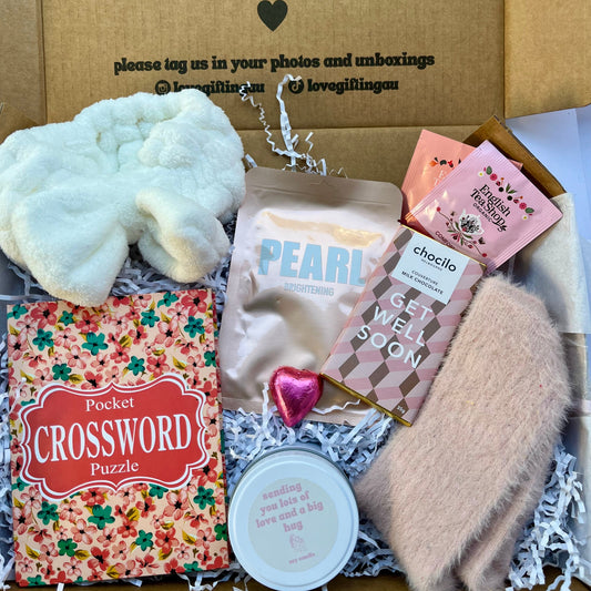 Get well soon recovery gift box which includes crossword book, facemask sheet, hug candle , teabags, pink fluffy socks , heart chocolate, toweling Headband.