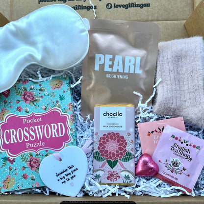 Gifting box with items including a sock, tea bags, and a crossword puzzle