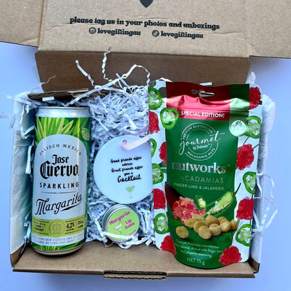 Gift box with a can of Jose Cuervo Margarita, a bag of snacks, and a card on a light blue background.
