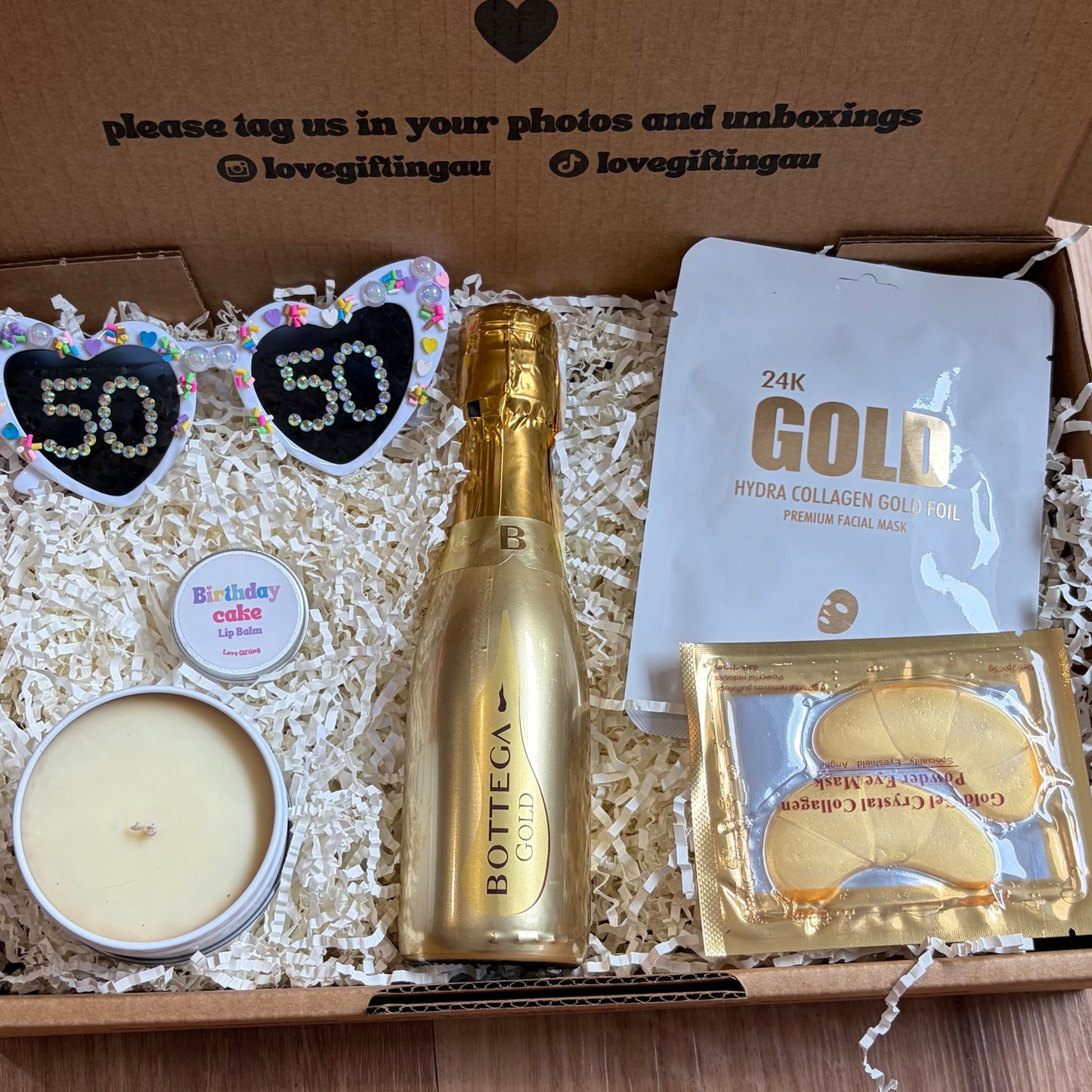 Gift box with champagne, candles, and other items on a wooden surface