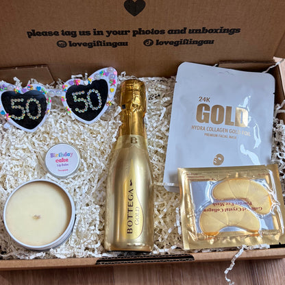 Gift box with champagne, candles, and other items on a wooden surface