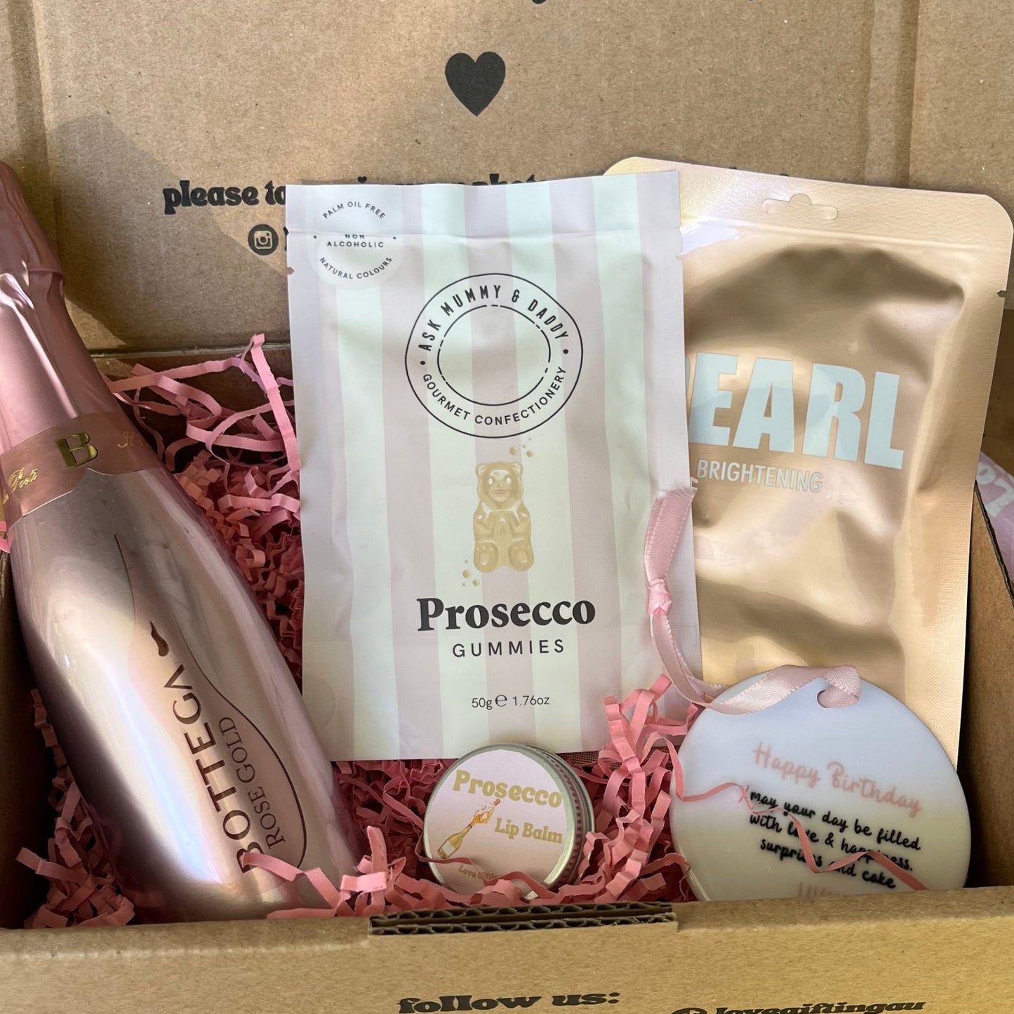Gift box with Prosecco gummies, a bottle-shaped container, and other items on a wooden surface.