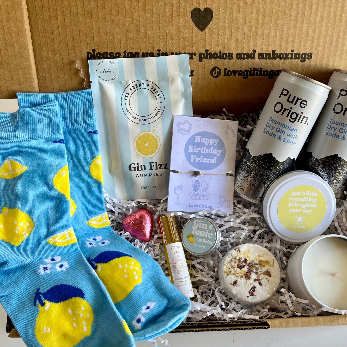 Gift box with blue lemon-patterned socks, gummy bears, and other items on a white background