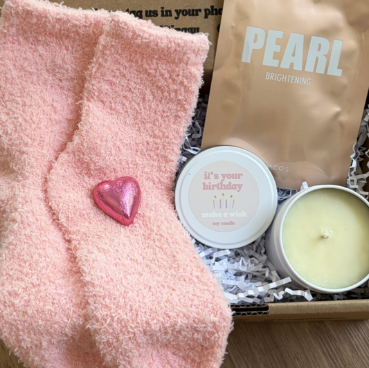 Pink fuzzy socks with a heart charm, a candle, and a product labeled 'Pearl' in a box.