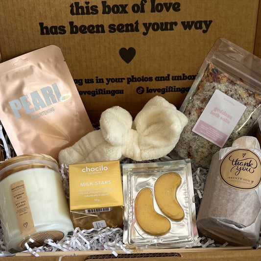 Gift box with various items including a candle, face masks, and a bag of tea, with a message on the box.